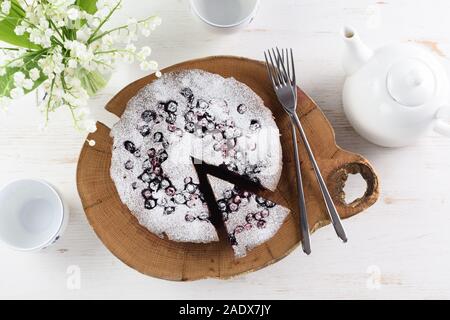 Homemade berry cake with bird cherry flour in icing sugar. Tasty bird cherry cake served with white teaware and lily of the valley flowers on white ba Stock Photo