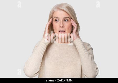 Headshot of aged woman feeling scared isolated on gray background Stock Photo