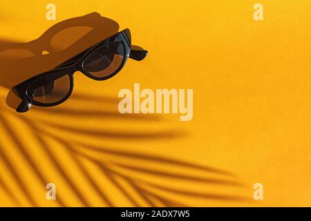 Top view hat and sunglasses on yellow background with sunlight and shadow of coconut leaves. travel concept Stock Photo
