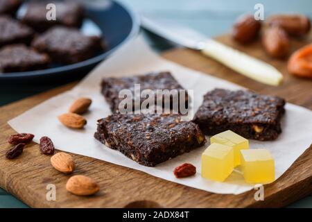 Vegan sweets. Brownies with almonds and agar jelly cubes served with raw almonds and dried fruits on wooden board closeup Stock Photo