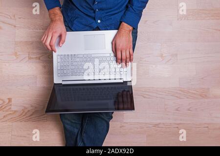 Young modern businessman or freelancer sitting on the floor with laptop on his knees, Stock Photo