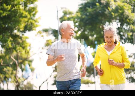 happy asian senior couple running exercising outdoors in park Stock Photo