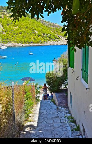 A pretty view down a path leading to the beach at the beautiful fishing village of Assos. Woman at bottom of steps looking out over bay. Stock Photo
