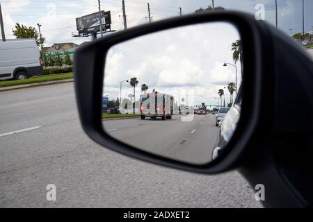 looking in side view rear mirror of approaching fire trucks on highway in florida usa Stock Photo