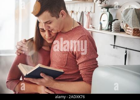 Some interesting information. Cute couple reading book together at home in the kitchen at daytime Stock Photo