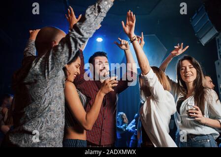 Raise your hands up. Happy people dancing in the luxury night club together with different drinks in their hands Stock Photo
