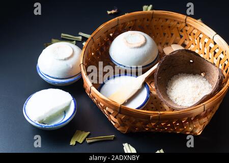 Food dessert concept Thai dessert Kanom Tuay Coconut Rice and pandan Custard in small porcelain cup and bamboo bastket on black background with copy s Stock Photo