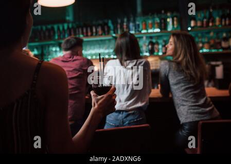 Girl with glass is going to the friends. Beautiful youth have party together with alcohol in the nightclub Stock Photo