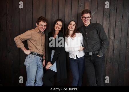 In the restaurant room. Youth stands against black wooden wall. Group of friends spending time together Stock Photo