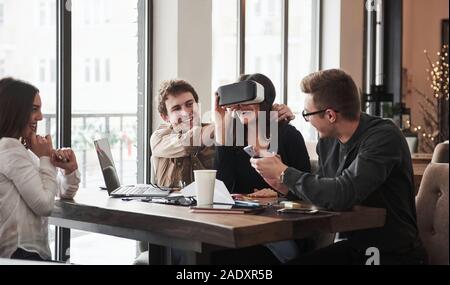 Guy helps girl to wear the virtual glasses Having fun in the office room. Friendly coworkers playing around at their break time Stock Photo