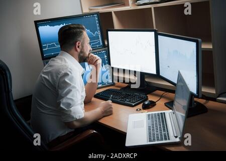 Modern office worker. Bearded man in white shirt sitting in the room with multiple computer screens in index charts Stock Photo