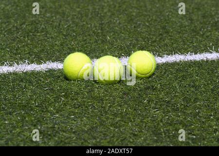 Three yellow tennis balls lays in-line on green synthetic court grass marked with white lines Stock Photo