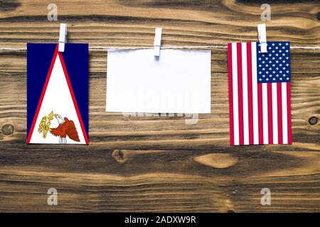 Hanging flags of American Samoa and United States attached to rope with clothes pins with copy space on white note paper on wooden background.Diplomat Stock Photo