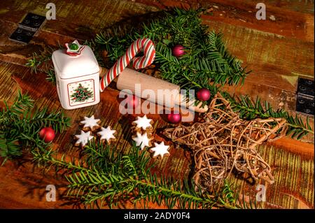 Christmas scene with cinnamon stars, rolling pin, candy cane, fir, christmas tree balls and a ceramic biscuit tin on an old wooden table. Stock Photo