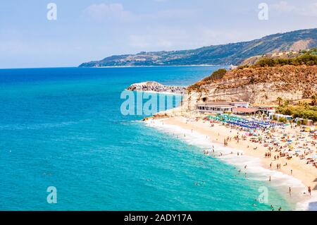 Landscape view on famous Rotonda Beach full of resting sunbathing and swimming people. Popular sea promenade in Tropea city in Italy