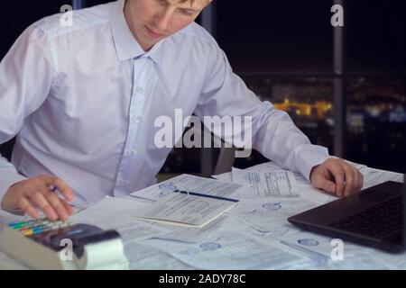A businessman works with stocks, bonds, obligations, securities and documents in a night office. Fulfillment of obligations to work with documents in Stock Photo