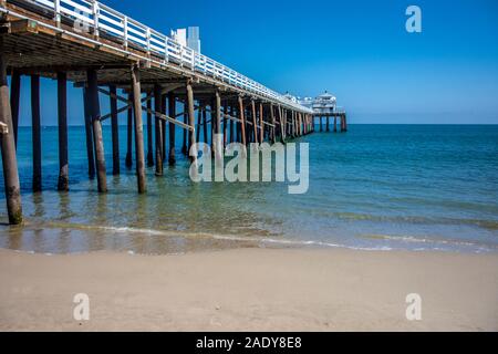 Calm seas and ocean pier connect with sandy beach on beautiful blue sky day next to Pacific Ocean in California Stock Photo