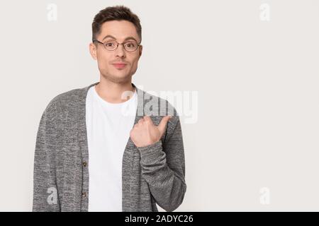 Millennial man pointing big finger to left isolated on gray Stock Photo