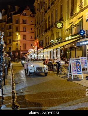 A Citroen 2CV driving down a street with cafes in the Latin Quarter of Paris at night Stock Photo