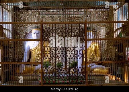 Two statues of the seated Buddha in a small village temple with ornate decoration behind a gilded cage in northwestern Myanmar (Burma) Stock Photo