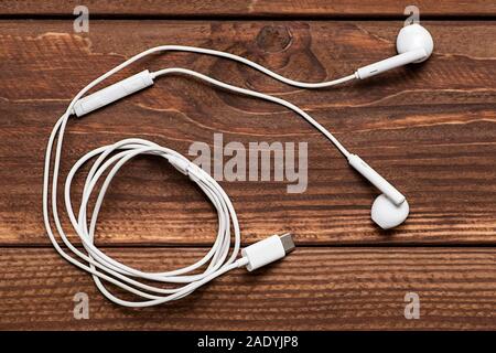 Modern white earphone, white in ear headphone on wooden table. White earphones over wooden board. Stock Photo