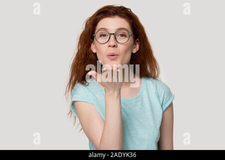 Millennial red-haired woman in eyeglasses sending air kisses. Stock Photo