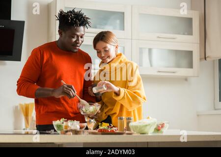 Peaceful couple smiling and adding salt to their salad Stock Photo