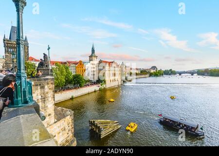 A young woman relaxes on the Charles Bridge as pedal and tourist boats cruise alongside the swans in the Vltava River in Prague, Czechia.