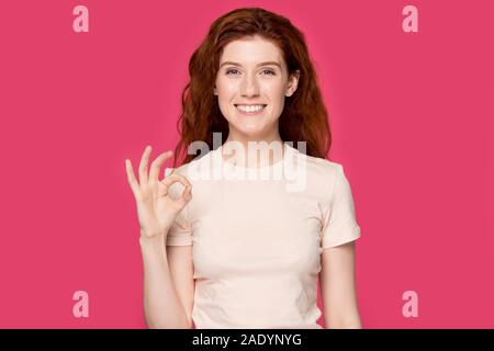 Happy millennial red-haired woman looking at camera, showing ok gesture. Stock Photo