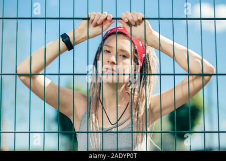 Calm lady putting both hands on the chain link fence and looking serious Stock Photo