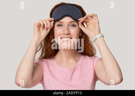 Happy millennial red-haired woman holding sleeping eye mask on forehead. Stock Photo