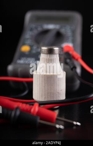 Electric meter and ceramic fuse. A device for measuring electric current and checking components. Dark background. Stock Photo