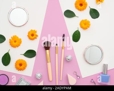 Fresh flower and green leaves on white papers and natural cosmetics, and makeup tools and brushes, mirror isolated on a pink background. Frame made of Stock Photo
