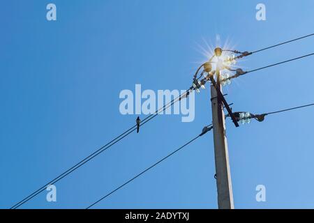 Close up of an overhead electricity pole and the cables and connections against a blue summer sky. Stock Photo