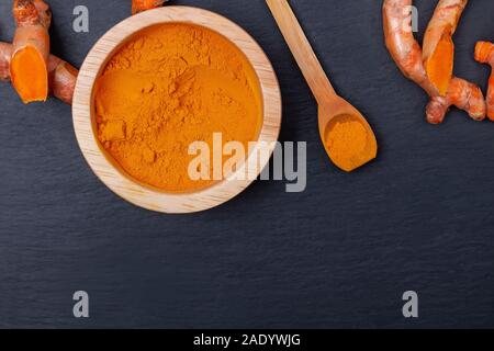 Turmeric powder in wooden bowl and roots on black stone background, Stock Photo