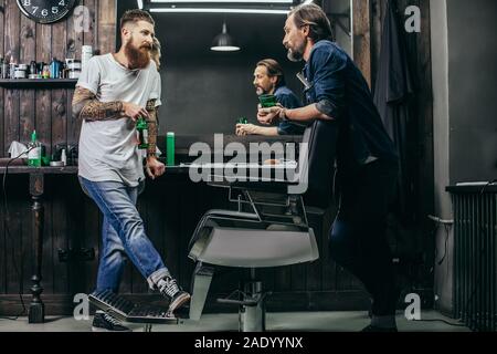 Two bearded men drinking beer while talking in barbershop Stock Photo