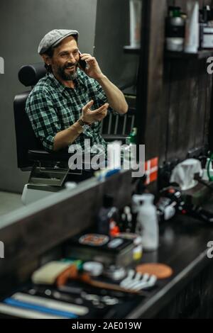 Emotional man smiling and talking on the phone while being in barber shop Stock Photo