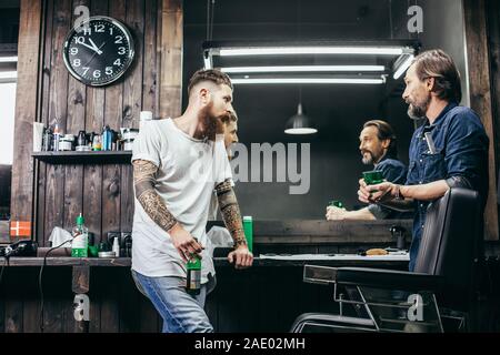 Curious man looking at his colleague while drinking beer with him Stock Photo