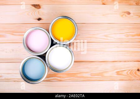 Four open cans of paint on wooden natural background. Yellow, white, pink, turquoise colors. Top view. Stock Photo
