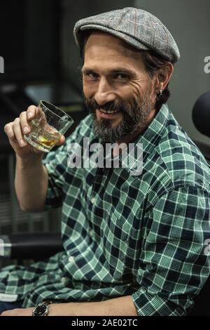 Positive man in checkered shirt smiling and drinking whiskey Stock Photo