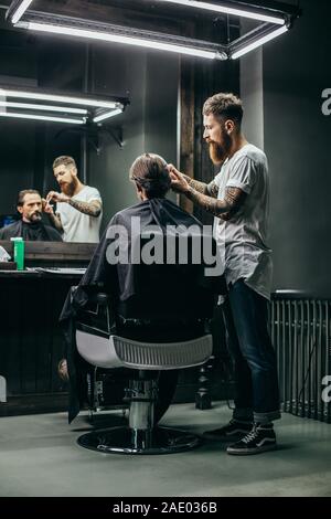 Full length of barber doing haircut for his visitor Stock Photo
