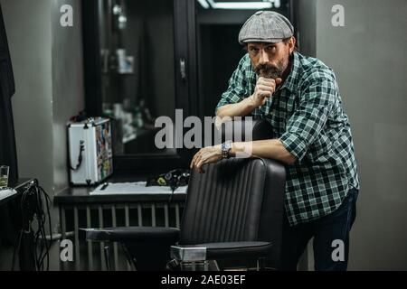 Thoughtful man leaning to the barber chair and touching his chin Stock Photo