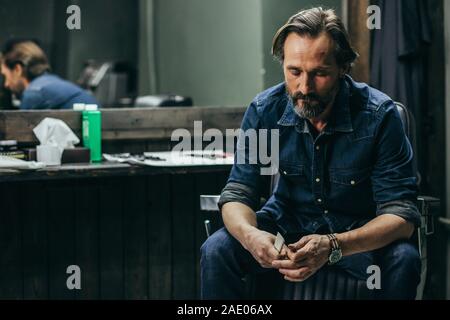Bearded man looking tired while sitting with comb in hands Stock Photo