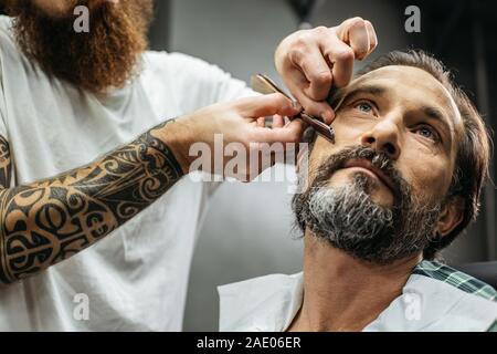 Close up of bearded man and careful barber using straight razor Stock Photo