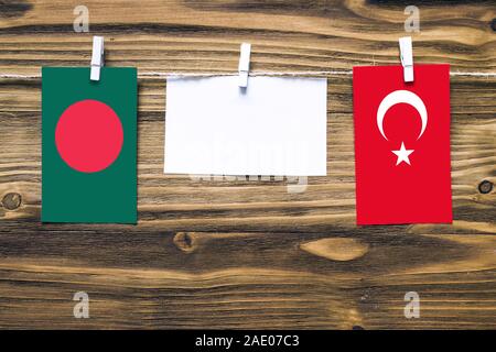 Hanging flags of Bangladesh and Turkey attached to rope with clothes pins with copy space on white note paper on wooden background.Diplomatic relation Stock Photo