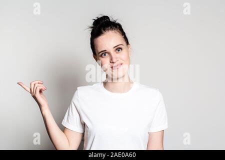 Attractive, young woman points a finger to the side, smiles sweetly and looks friendly at the camera. Stock Photo