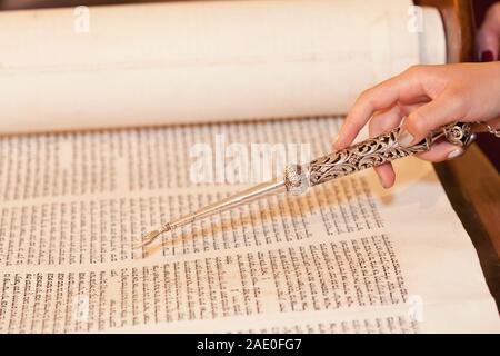 Young Jewish woman holding a yad, reading an ancient Torah scroll during her Bat Mitzvah ceremony Stock Photo