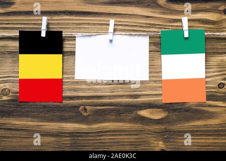 Hanging flags of Belgium and Ireland attached to rope with clothes pins with copy space on white note paper on wooden background.Diplomatic relations Stock Photo