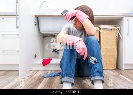 Woman sitting near leaking sink calling for help Stock Photo