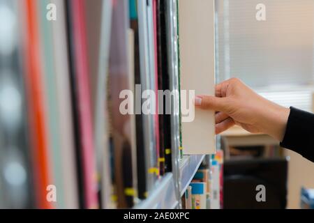 Young student picking a book from the shelf in the library. Preparing for exams, young man searching for or choosing a book in the public library in u Stock Photo